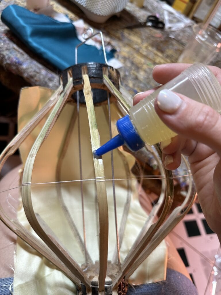 This image shows a person holding a bottle of glue and putting the glue on a wooden lantern