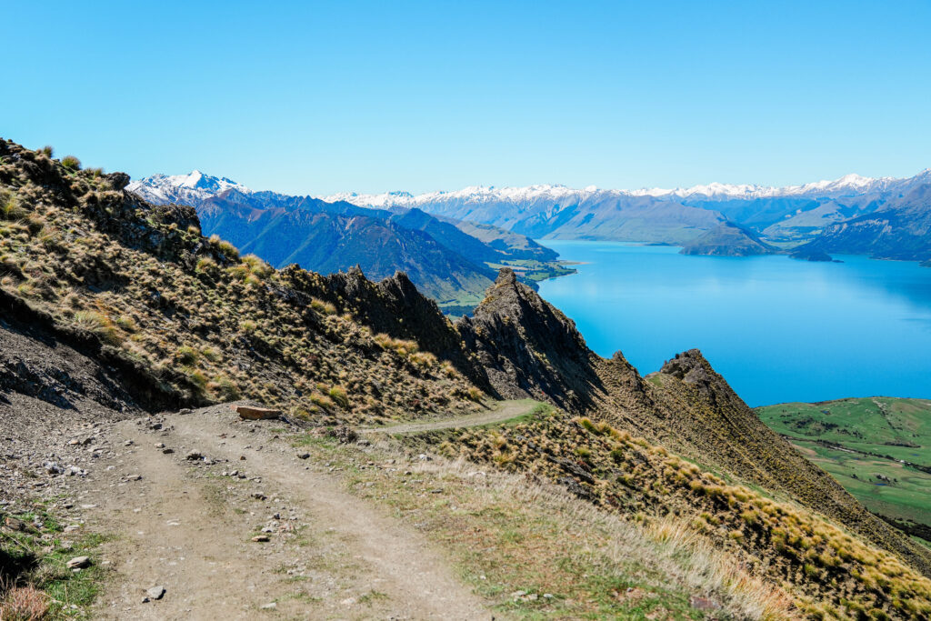 a view of a snow covered mountains and an alpine lake with a dirt road in the foreground