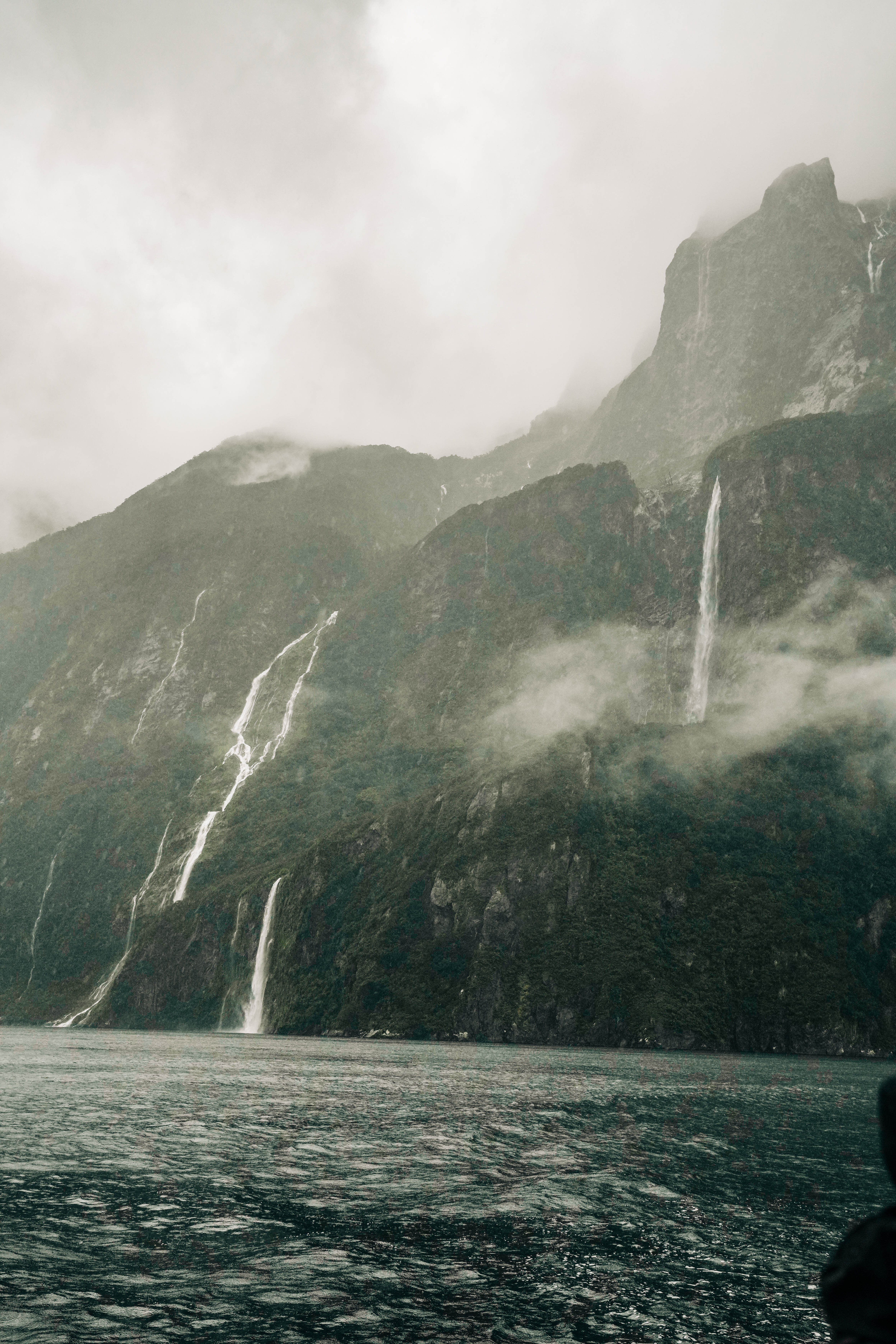 milford sound with water streaming town the fjords with a misty sky