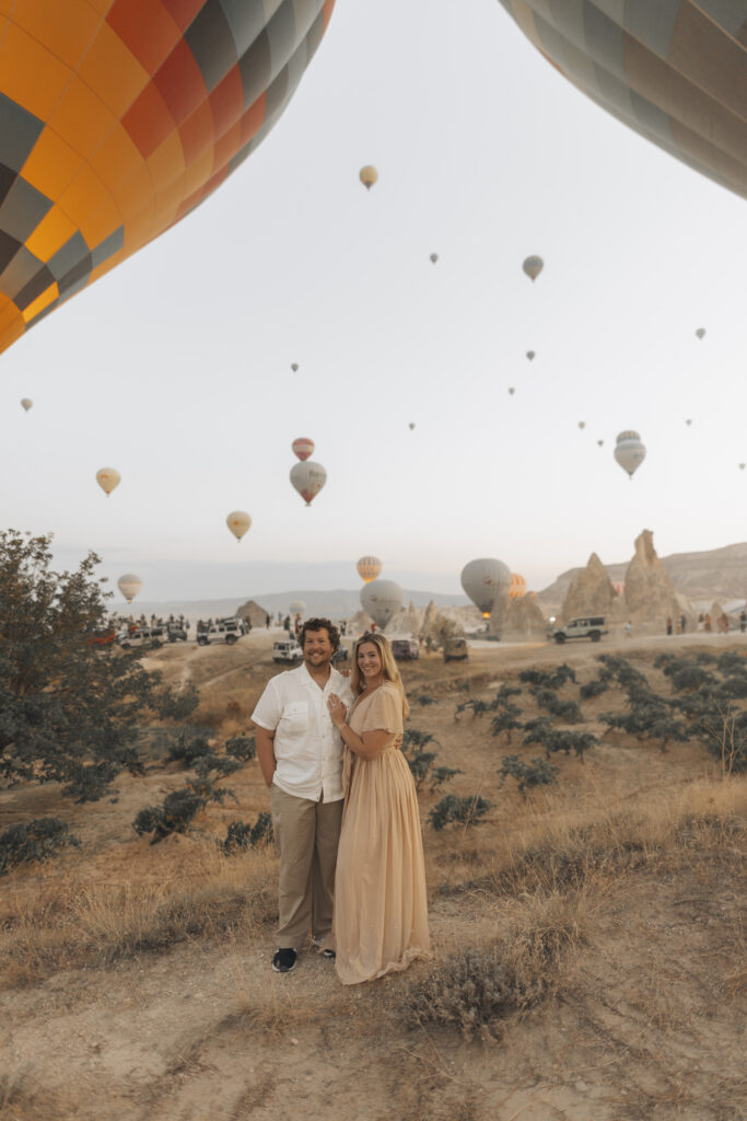 a couple posing with hot air balloons behind them