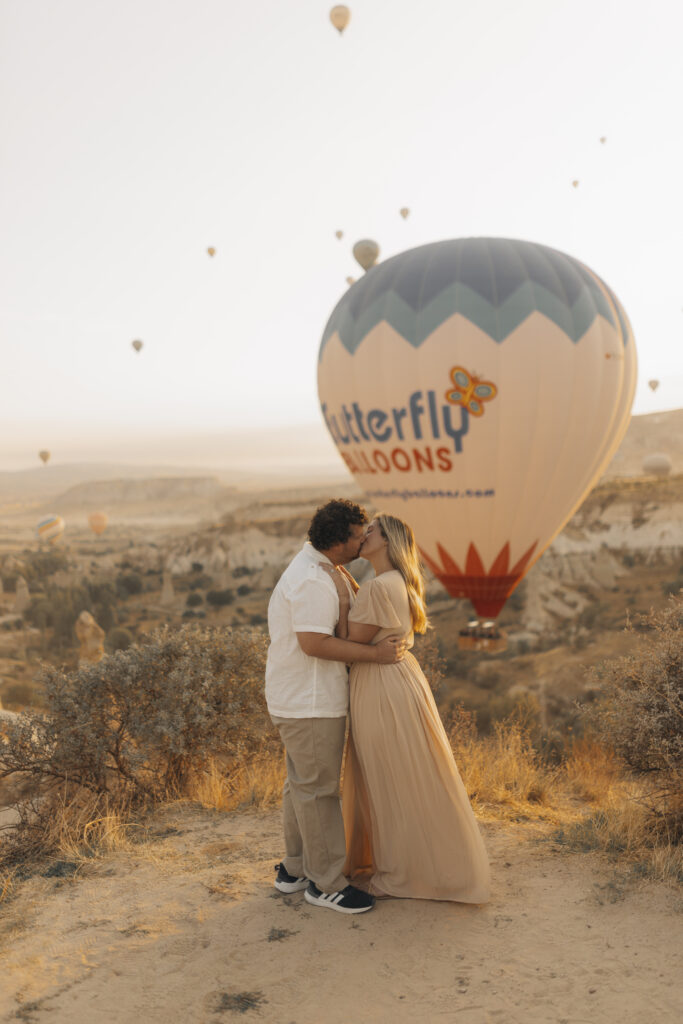 a couple kissing with a hot air balloon behind them