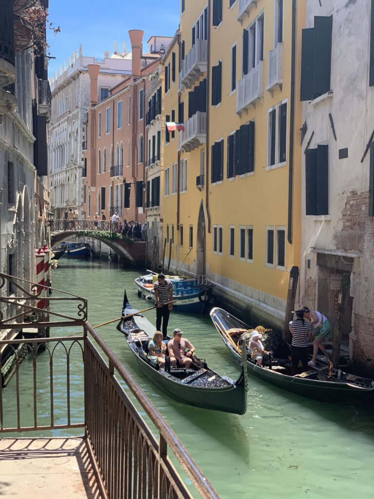 people riding in a gondola through the Venice canal with bright building surrounding them