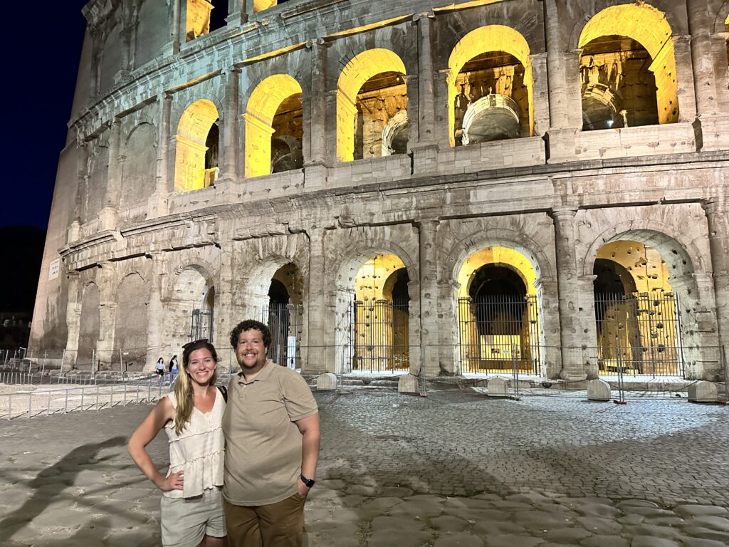 a couple standing in front of the Roman colosseum at night